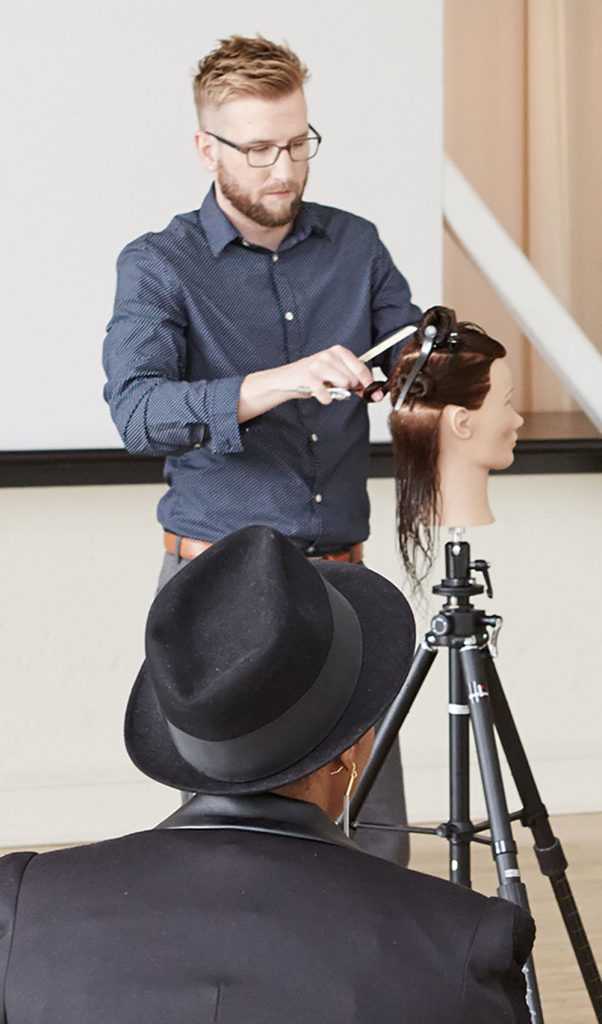 Pivot Point instructor showing students hairstyling techniques while another instructor recording with an ipad