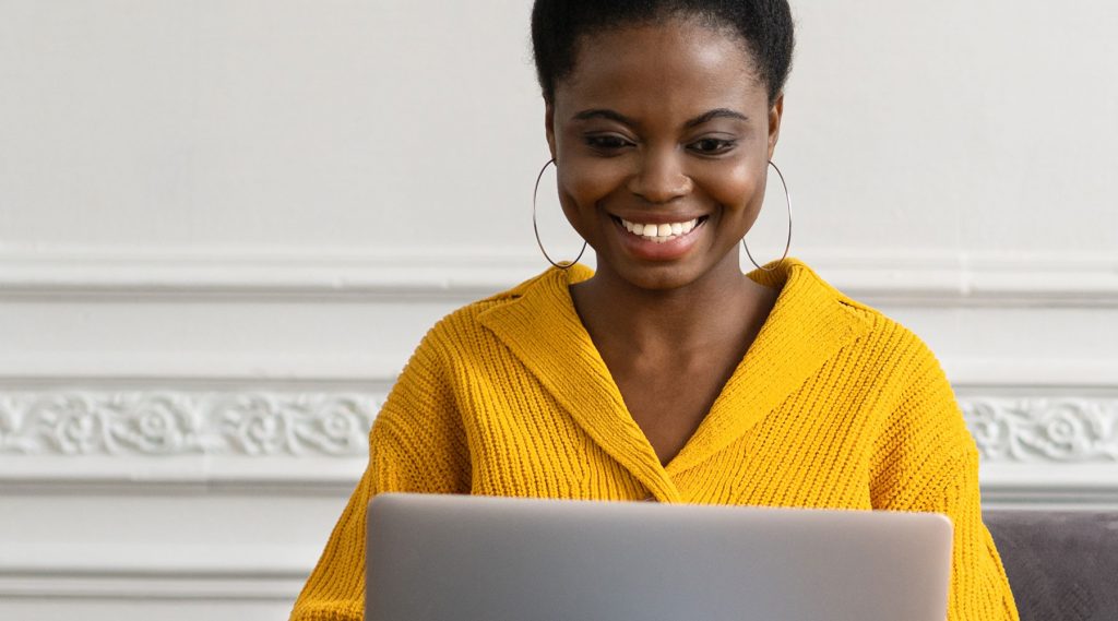 Young female wearing yellow sweater using a laptop.